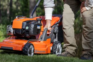 Eine Person, die die Einstellungen an einem Husqvarna Rasenmäher in einem Garten anpasst.