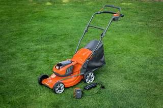 Χλοοκοπτικό με μπαταρία με συλλέκτη γρασιδιού σε γκαζόν, συνοδευόμενο από μπαταρία και φορτιστή.