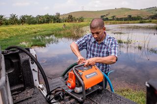 Чоловік, який встановлює водяний насос Husqvarna на кузові вантажівки біля озера.