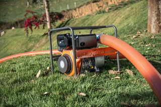 Водяний насос Husqvarna зі шлангами для роботи на трав'янистій ділянці.