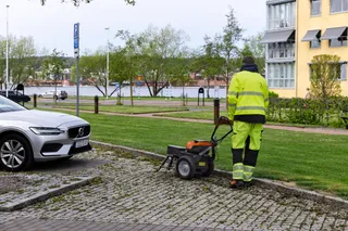 A person using a lawn aerator on a grassy area near a parked car.