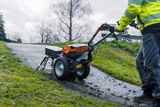 A person operating a walk-behind mower on a grassy slope.