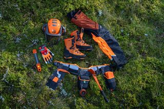 Collection d’équipements et d’outils de protection Husqvarna disposés sur l’herbe, y compris un casque de sécurité et un pantalon de travail.