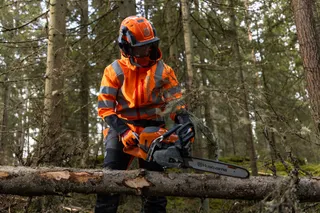 En person som använder en motorsåg från Husqvarna för att kapa ett nedfallet träd i en skog.