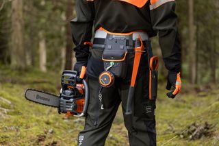 Personne tenant une tronçonneuse Husqvarna en forêt, portant des vêtements de travail.