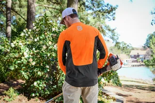 A person wearing work gear holding a Husqvarna product in a garden setting.