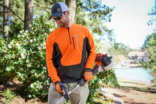 Une personne tenant une débroussailleuse Husqvarna dans un jardin.