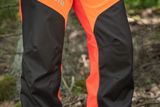 Person wearing Husqvarna chainsaw trousers in a forest setting.