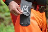 Inimene hoiab käes Husqvarna toodet, kes näitab tööpükste taskut.