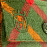 Närbild på ett grön- och orangerutigt tyg med broderad Husqvarnalogotyp och en knapp.