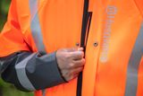 A person fastening the zipper of a Husqvarna work jacket.