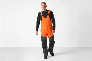 Person wearing work gear, including overalls, standing in a studio setting.