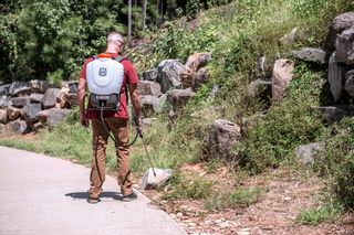 A person using a backpack sprayer to treat weeds along a rocky path.