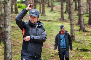 Two people wearing work gear walking through a forested area.