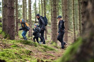 A group of people walking through a dense forest, wearing outdoor work gear.