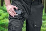Uma pessoa colocando um smartphone no bolso das calças de trabalho em um ambiente de floresta.