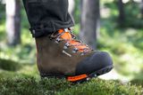 Close-up de uma pessoa usando botas de trabalho Husqvarna em pé sobre musgo em uma floresta.