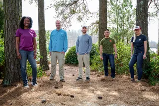 Cinq personnes debout parmi les pins dans un décor forestier.