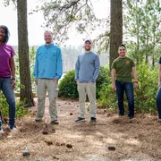 Cinq personnes debout parmi les pins dans un décor forestier.