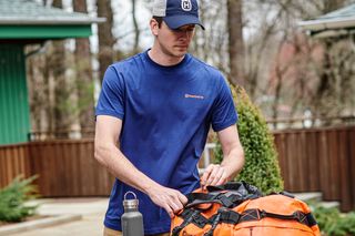 A person preparing a Husqvarna duffel bag on a wooden picnic table in an outdoor setting.
