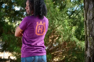 Personne de l’extérieur portant une chemise violette avec le logo Husqvarna, debout dans un décor forestier.