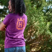 Personne de l’extérieur portant une chemise violette avec le logo Husqvarna, debout dans un décor forestier.