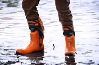 Person wearing waterproof work boots standing in shallow water.