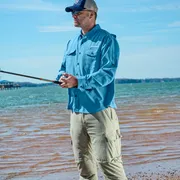 Une personne pêchant au bord d’un lac, avec un seau sur le rivage sablonneux.