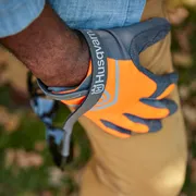 Une personne portant des gants de travail Husqvarna, tenant des lunettes de soleil à l’extérieur.