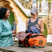 Deux personnes debout à l’extérieur avec un sac de sport sur une table en bois, l’une tenant une bouteille d’eau.