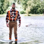 A person wearing work gear walking through shallow water in a forest setting.