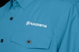 Vue rapprochée d’une chemise Husqvarna bleue avec poches boutonnées et logo brodé.