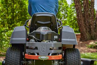 Rear view of a person operating a ride-on lawn mower in a garden.