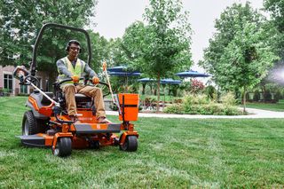 A person mowing lawn with a ride-on mower in a garden setting.