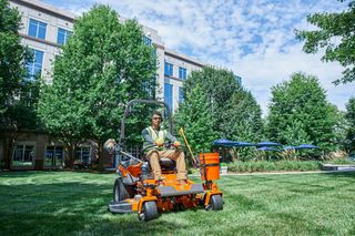 A person mowing lawn with a ride-on mower in a landscaped garden.