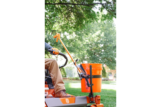 A person operating a ride-on mower equipped with a grass catcher in a garden.