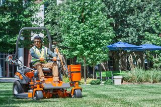 A person operating a ride-on lawn mower in a landscaped garden setting.