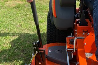 En person som använder en åkgräsklippare på gräs med fokus på spakmekanismen.