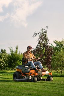 A person mowing lawn with a ride-on mower in a garden.