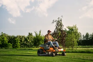 A person mowing lawn with a ride-on mower in a garden.