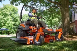 Une personne qui conduit une tondeuse à gazon autoportée sous un grand arbre dans un jardin.