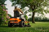A person mowing lawn with a ride-on mower in a garden.