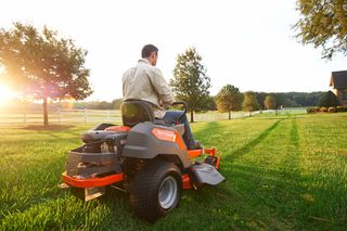 Una persona cortando el césped con un tractor cortacésped en un jardín durante la puesta de sol.