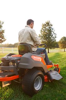 Persona, kas pļauj zālienu ar pļāvēju dārzā saulrieta laikā.