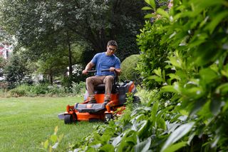 A person mowing a lawn with a ride-on mower in a garden setting.