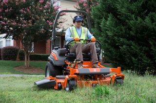 A person operating a ride-on mower, cutting grass in a residential garden.
