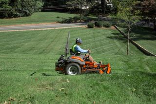 A person mowing lawn with a ride-on mower on a grassy slope.