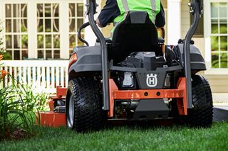 Une personne tond la pelouse avec une tondeuse autoportée dans un jardin, avec une maison en arrière-plan.