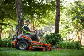 A person mowing lawn with a ride-on mower in a garden setting.