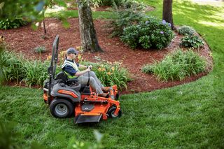 A person mowing a lawn with a ride-on mower in a well-maintained garden.